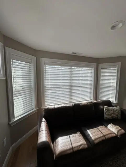 White blinds on a bay window behind a leather sofa