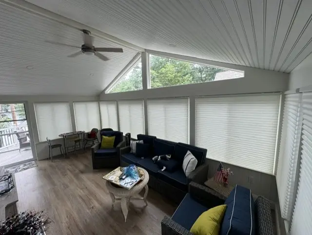 Sunroom wrapped in light cellular shades, with navy sofas under a vaulted ceiling